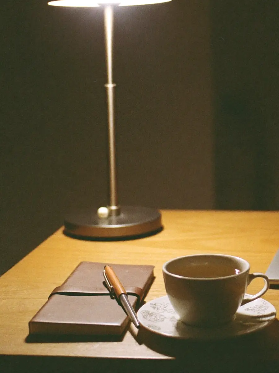 A desk late in the evening under a single lamp — a leather notebook, a pen and a cup of tea.