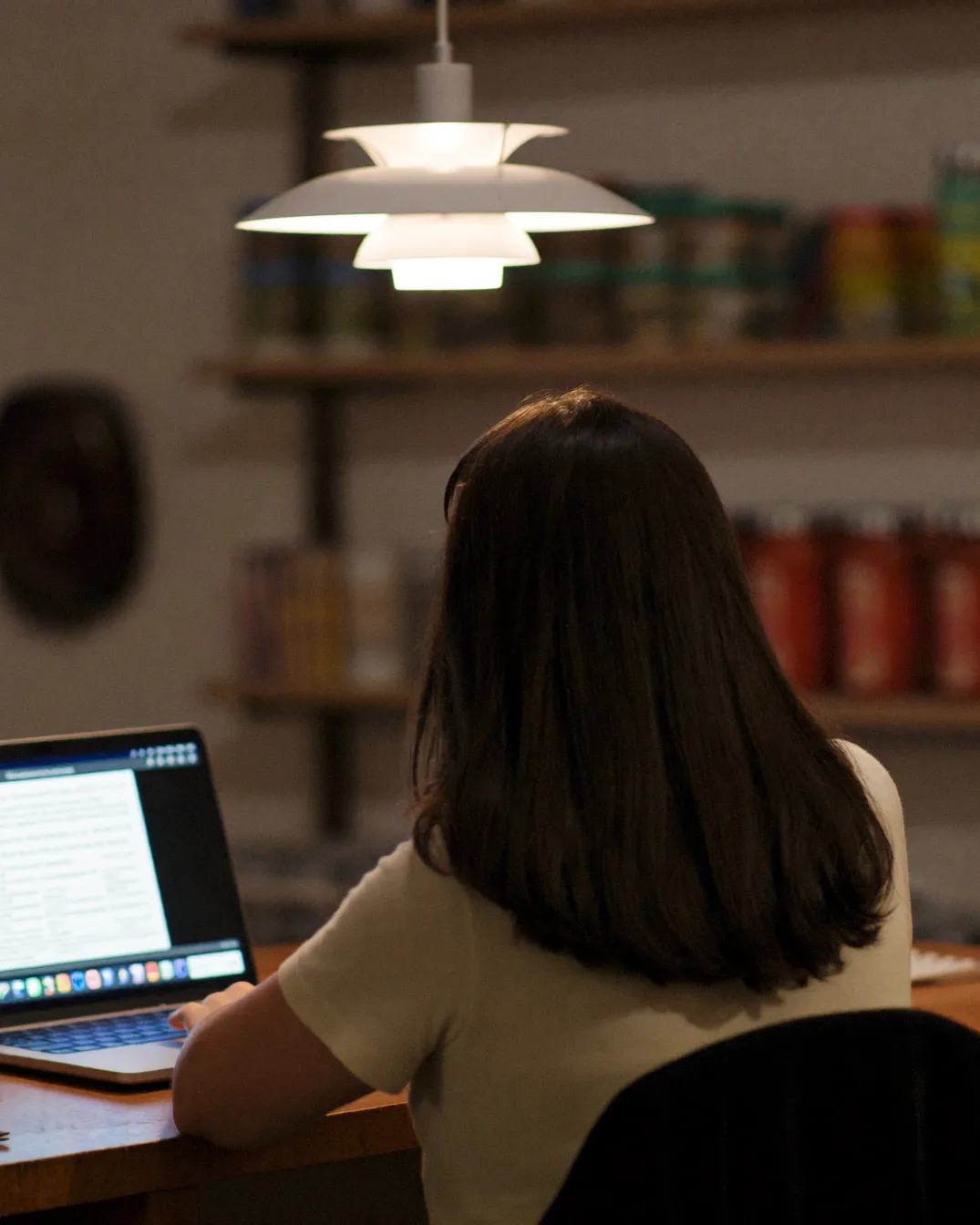 A local-business owner at her counter after close, still answering enquiries by lamplight