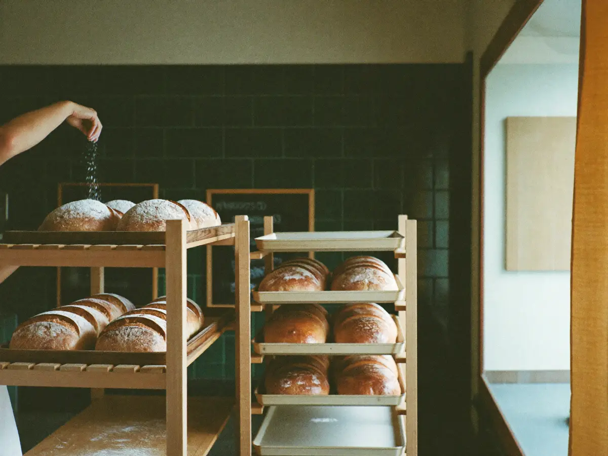 Trays of bread cooling on wooden racks in a small bakery.