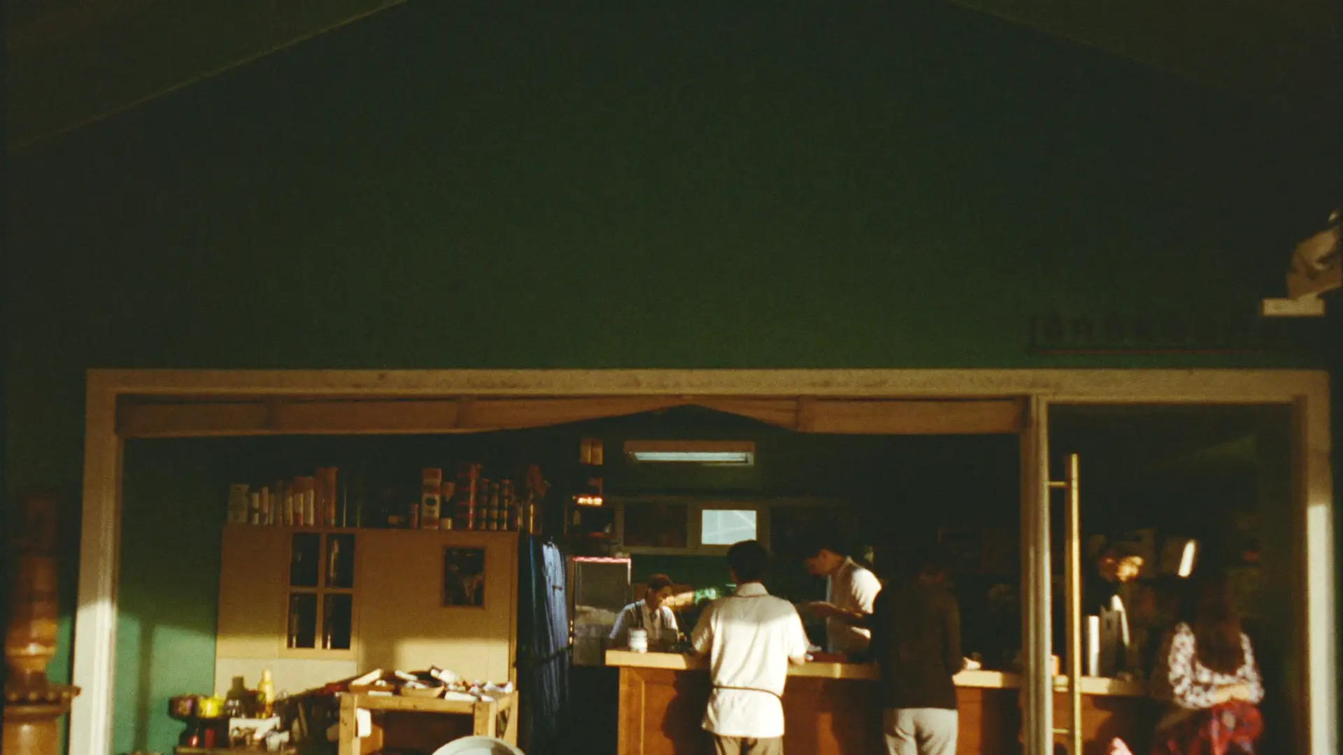 A small shop at its busiest hour, customers at the counter in golden light.