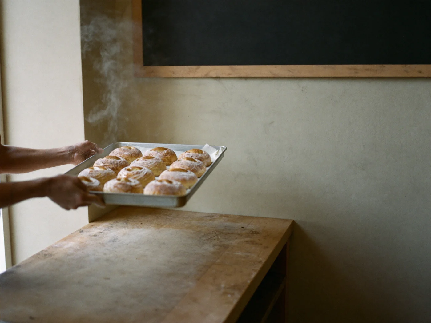 Hands sliding a tray of fresh bakes onto a workbench