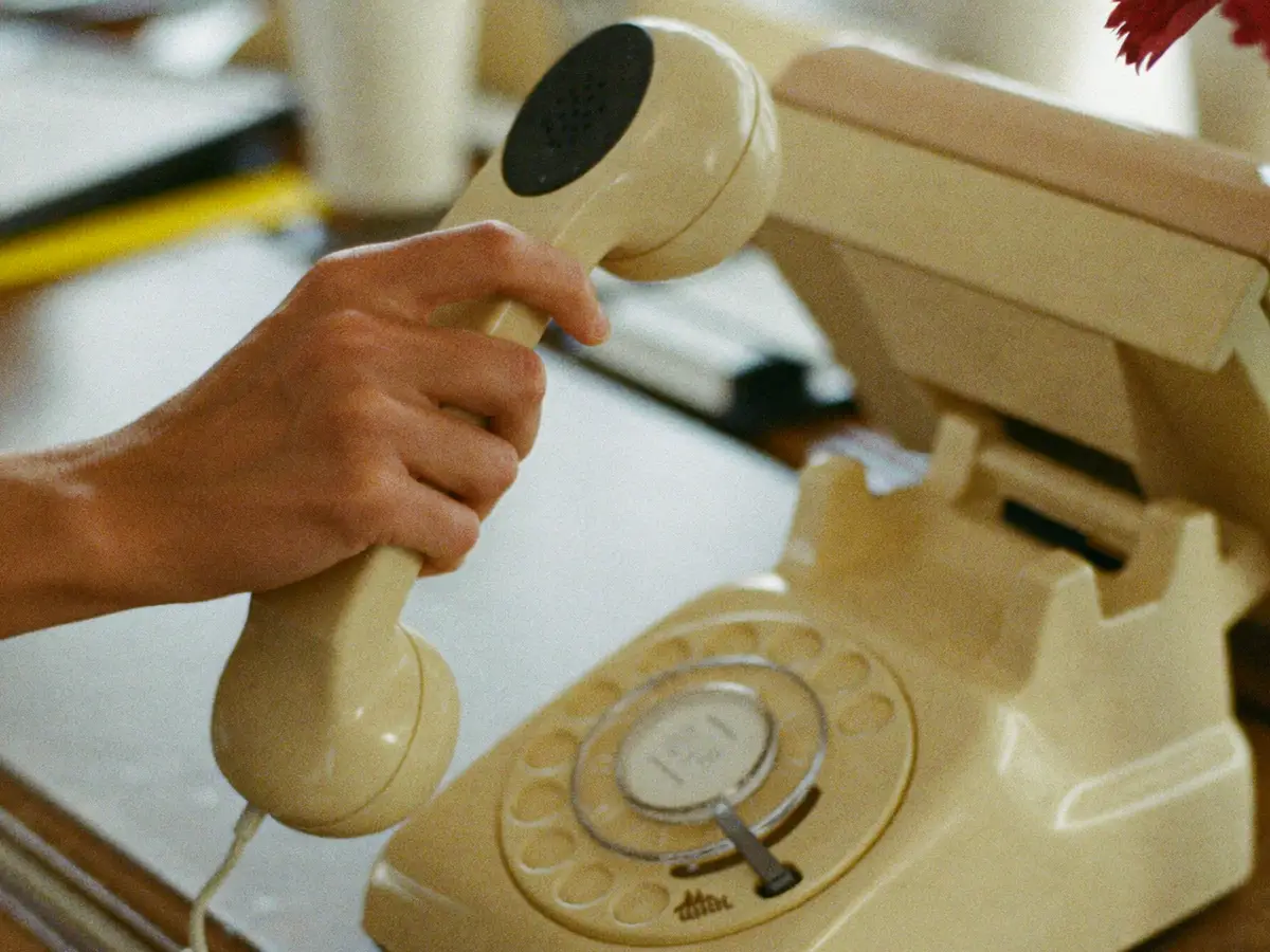 A hand lifting the handset of a cream desk telephone at a reception counter.