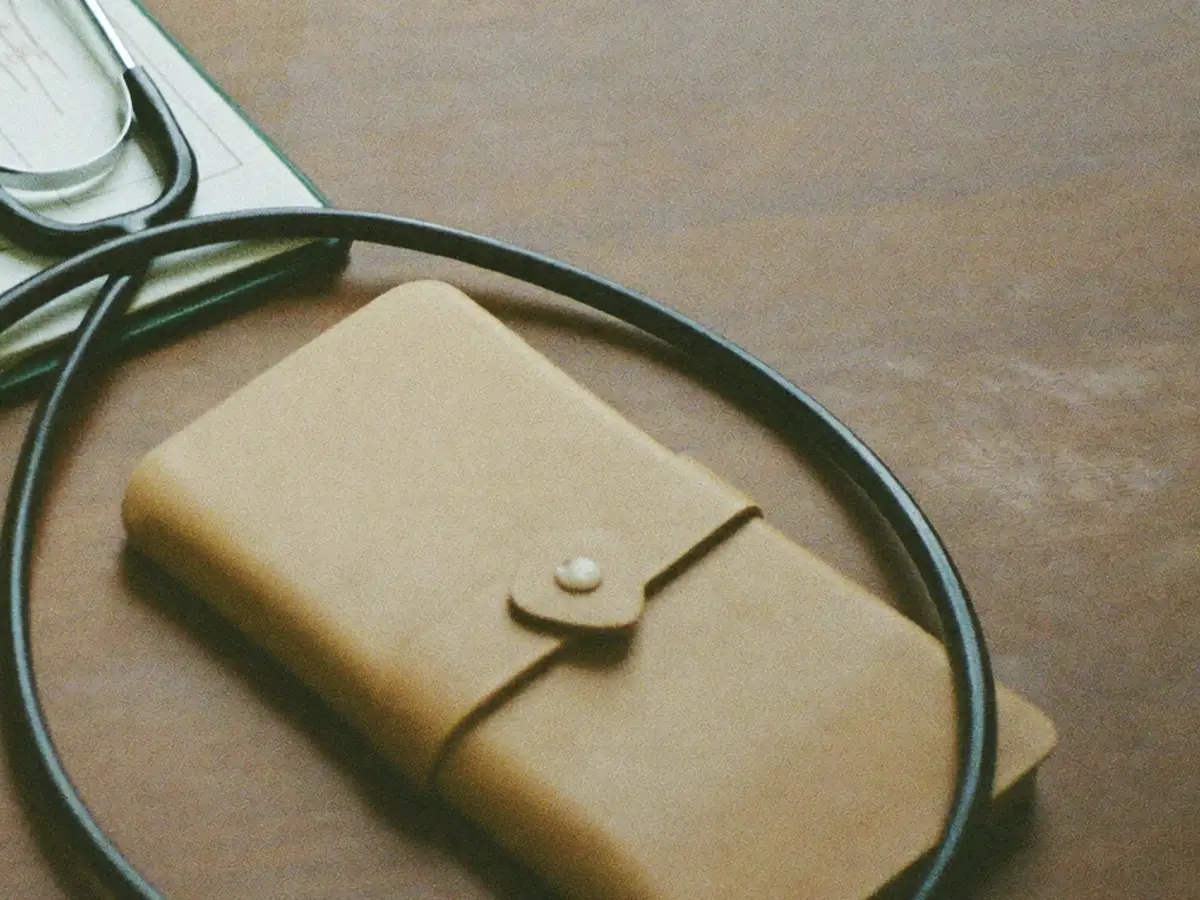 A stethoscope coiled beside a soft leather case on a clinician's desk.