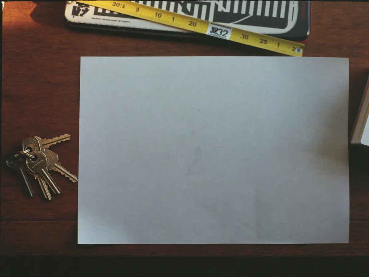 A set of door keys and a tape measure on a desk beside a blank sheet of paper.
