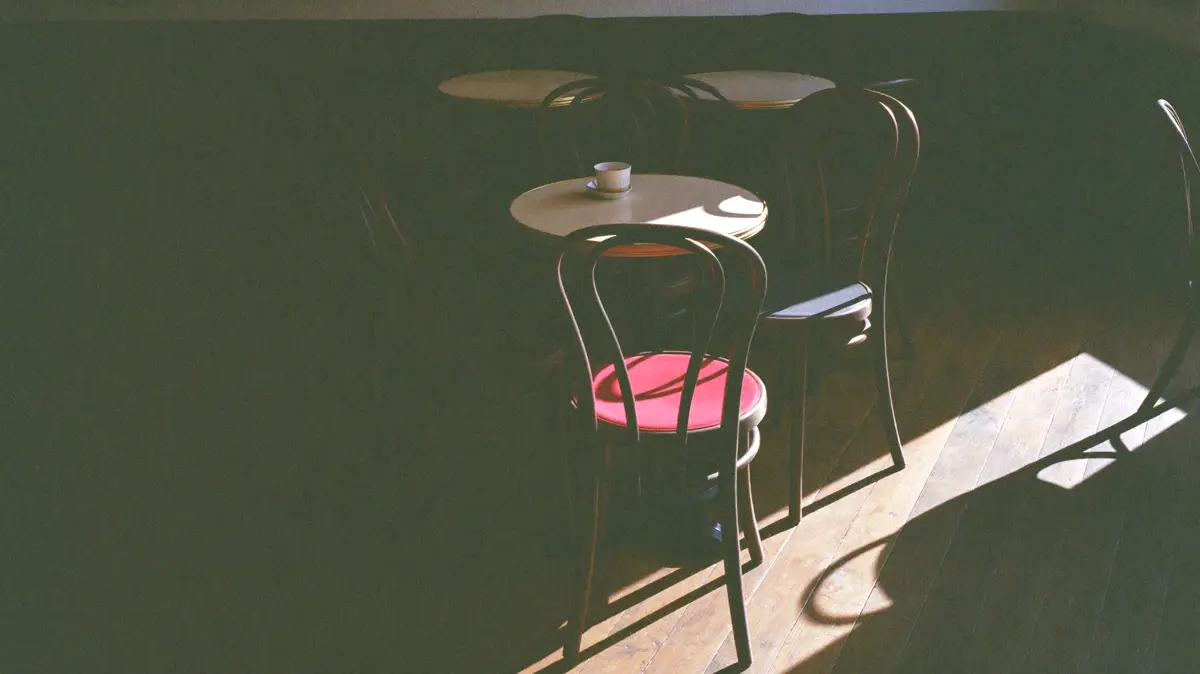Empty café tables and bentwood chairs in low midweek afternoon sun.
